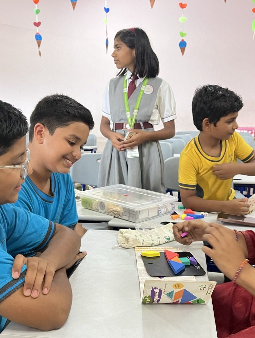 Children gathered at a table of materials while one girl presents to the group