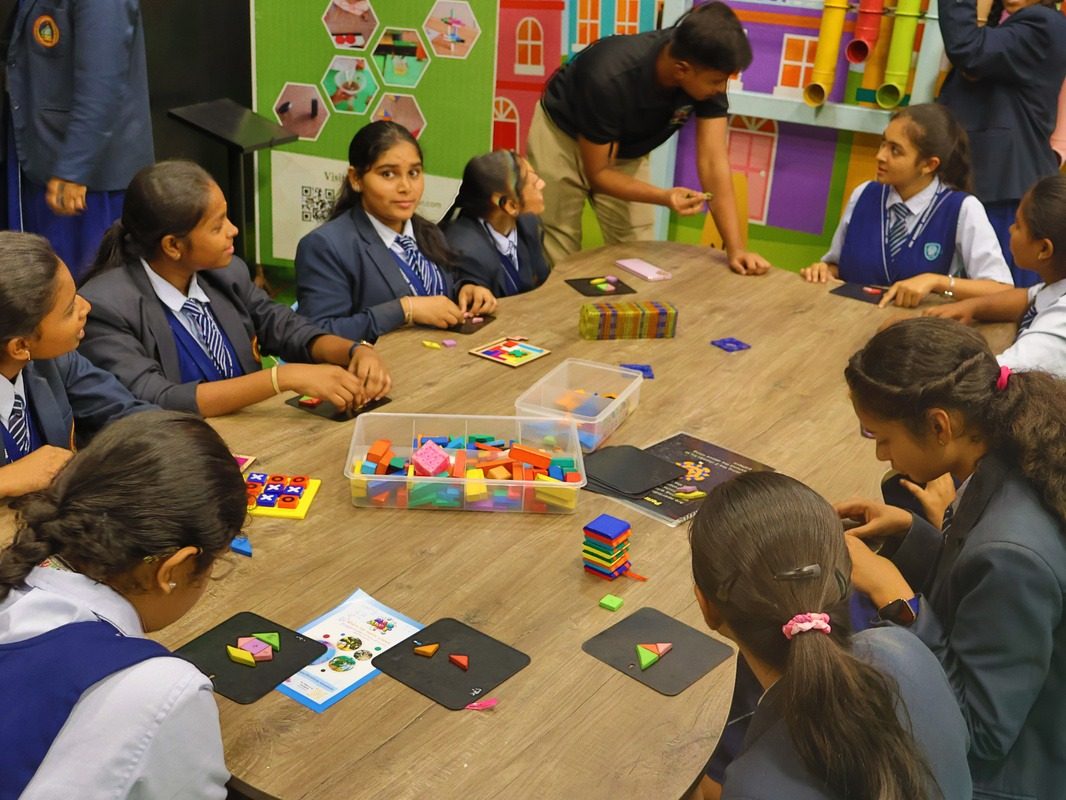 Middle-school children sorting shape cards and manipulatives around one table while a facilitator leans in