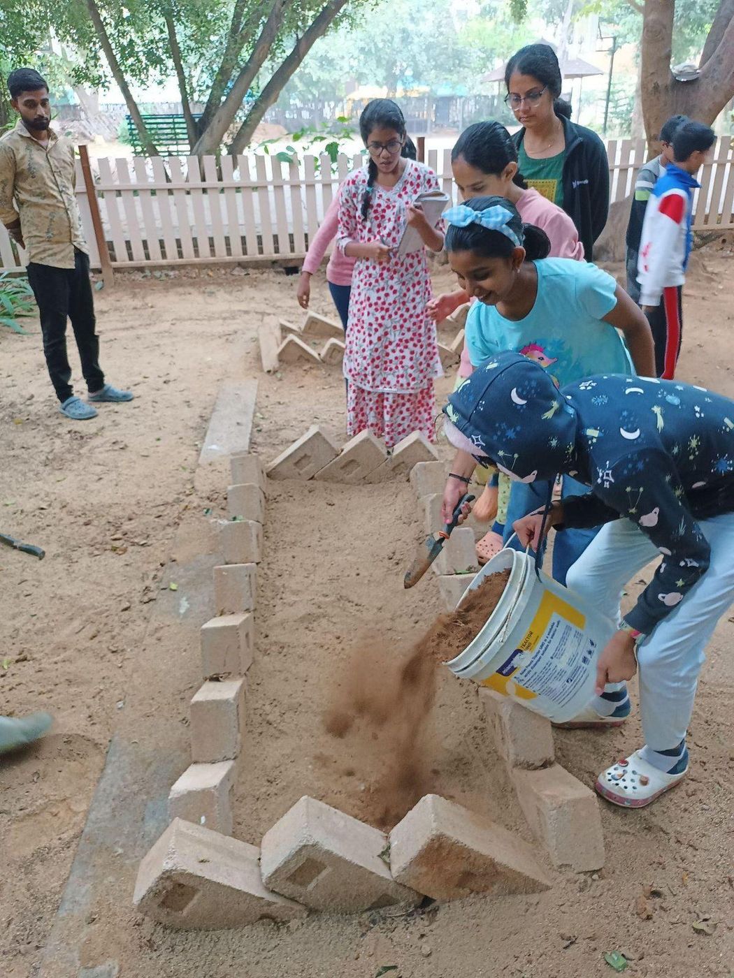Children and adults laying out and building raised garden beds in a school ground