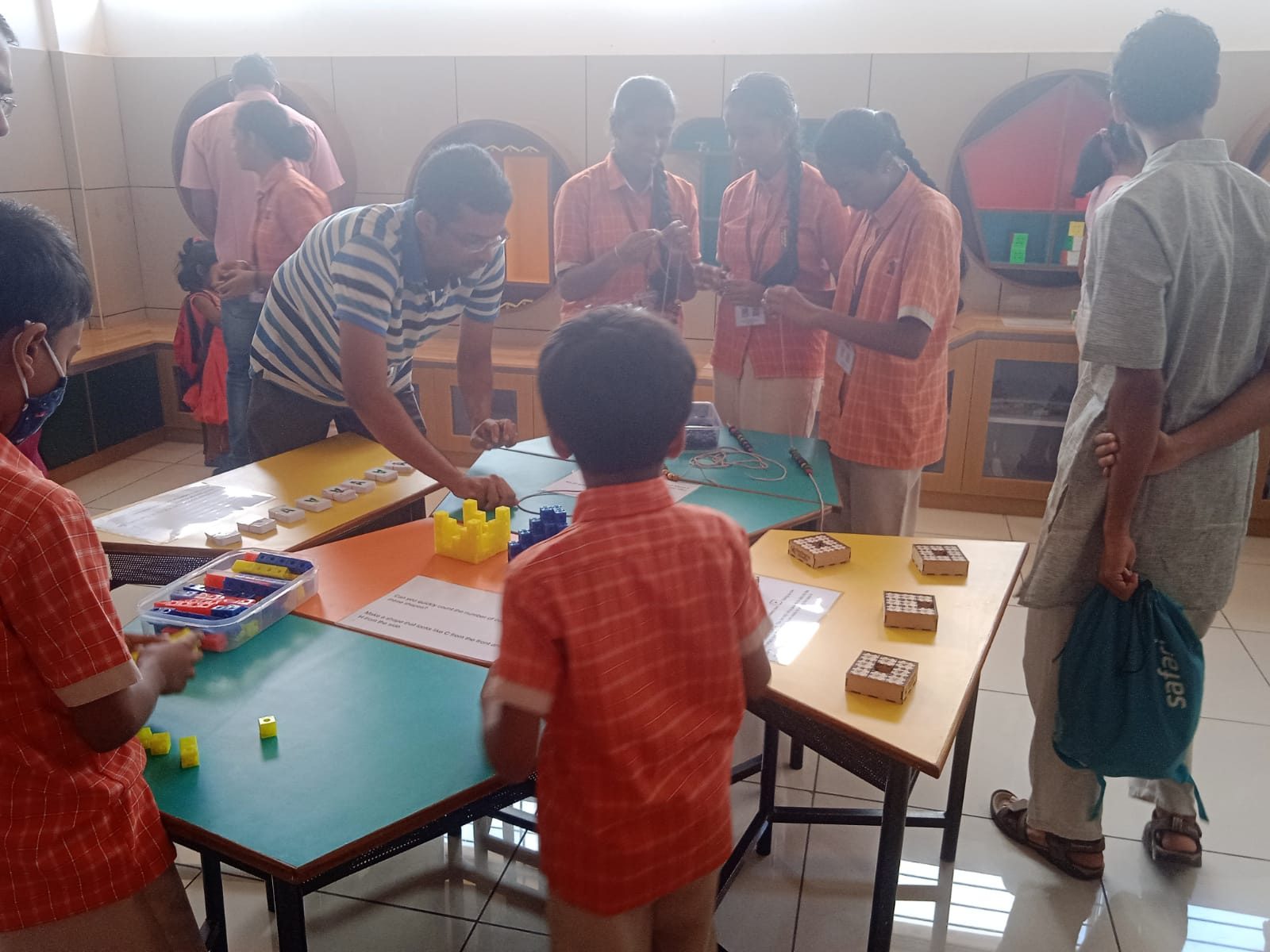 Children in uniform at tables laid out with kits and materials, a facilitator working alongside them