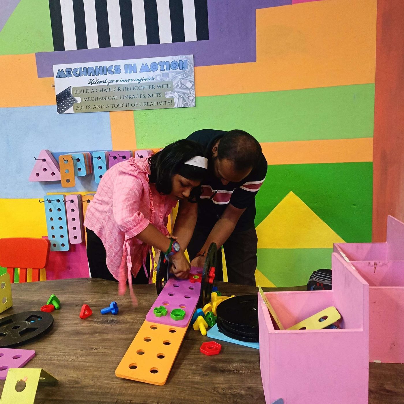 Two children bolting together a structure from a construction set of oversized nuts, bolts and beams