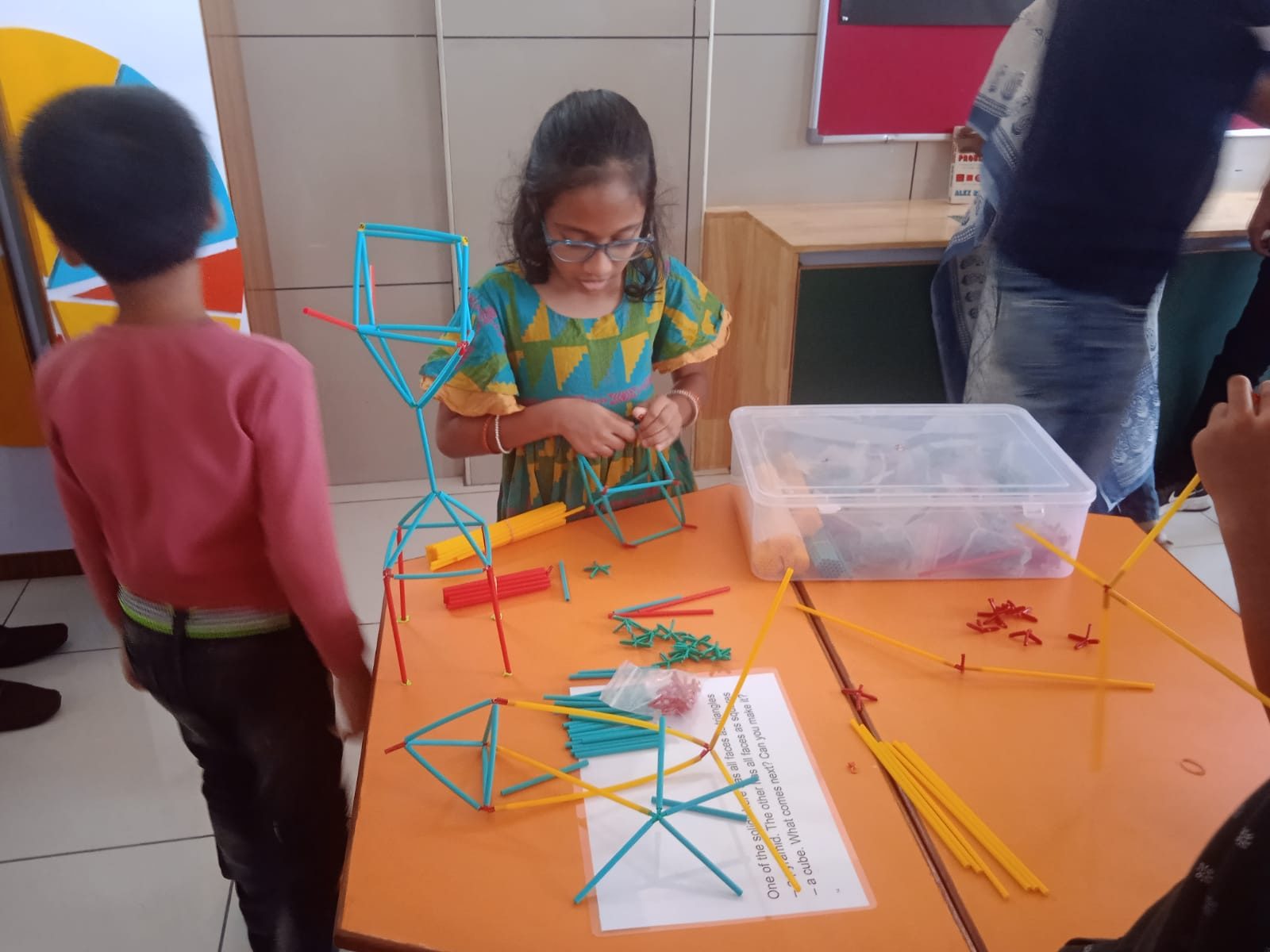 Children building three-dimensional structures out of straws and connectors on a workbench